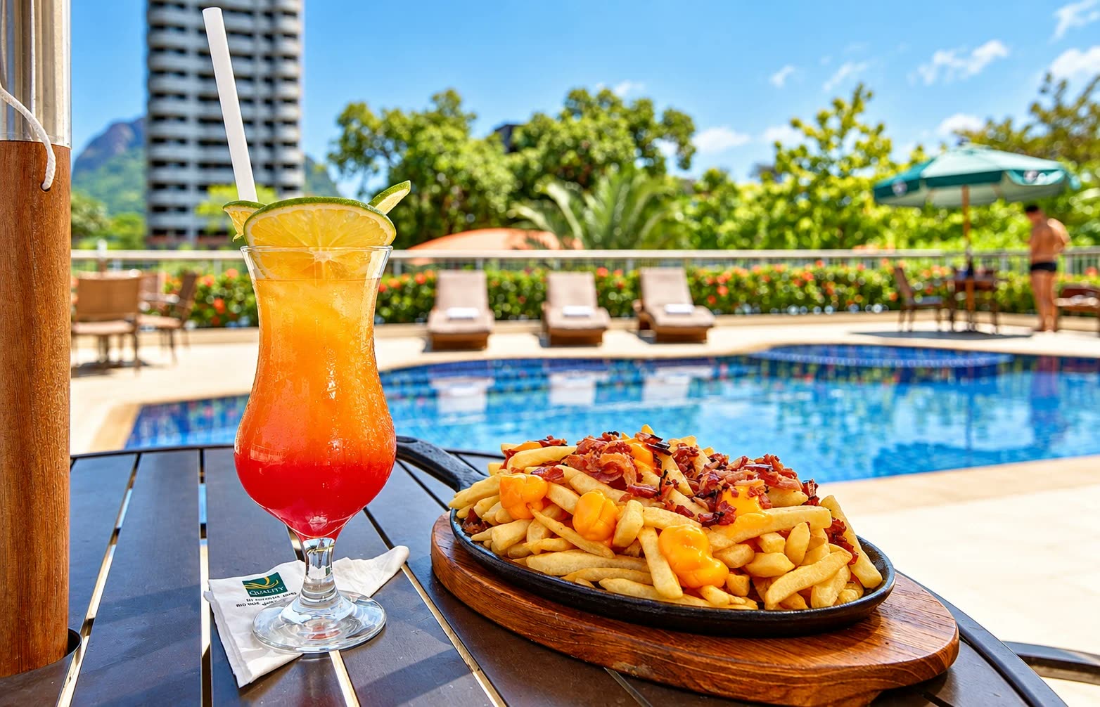 Drinque e porção de batata frita numa mesa à beira da piscina