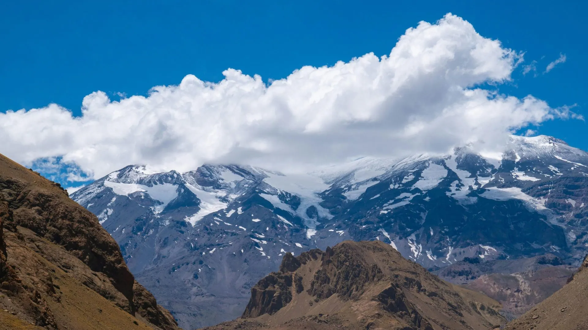 Picos nevados da Cordilheira dos Andes sob nuvens brancas e céu azul