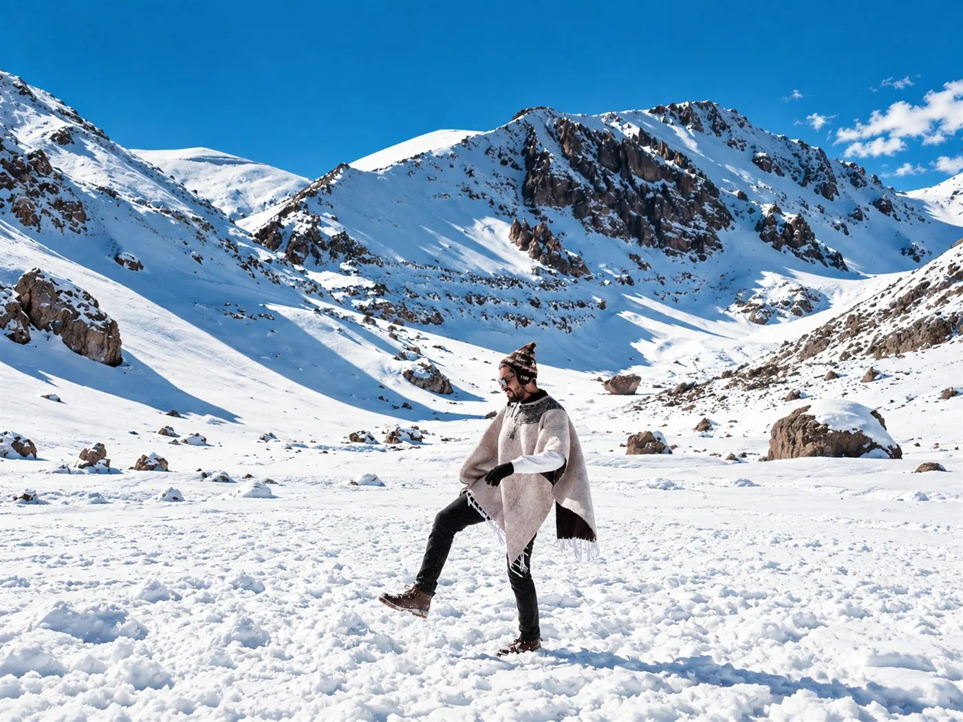 Viajante com poncho e gorro na neve, com montanhas ao fundo