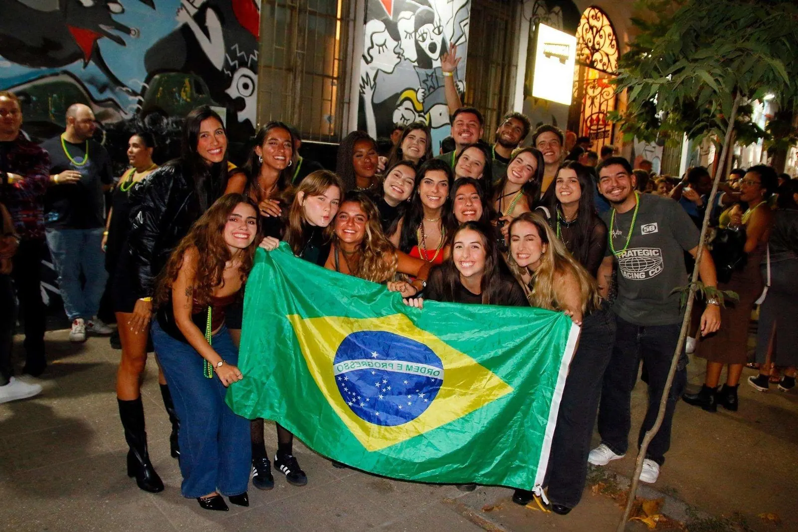 Grupo de brasileiros sorrindo com a bandeira do Brasil em uma noite em Santiago