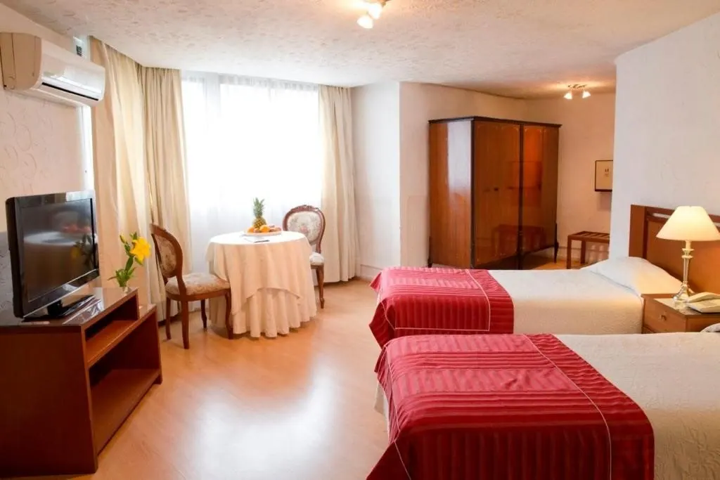 Quarto do Hotel Montecarlo Santiago com duas camas de solteiro e mesa redonda