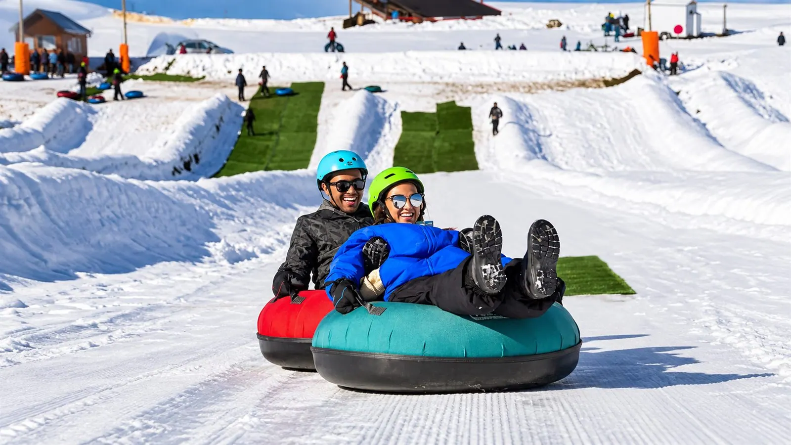 Duas pessoas descendo a pista de neve em boias de tubing