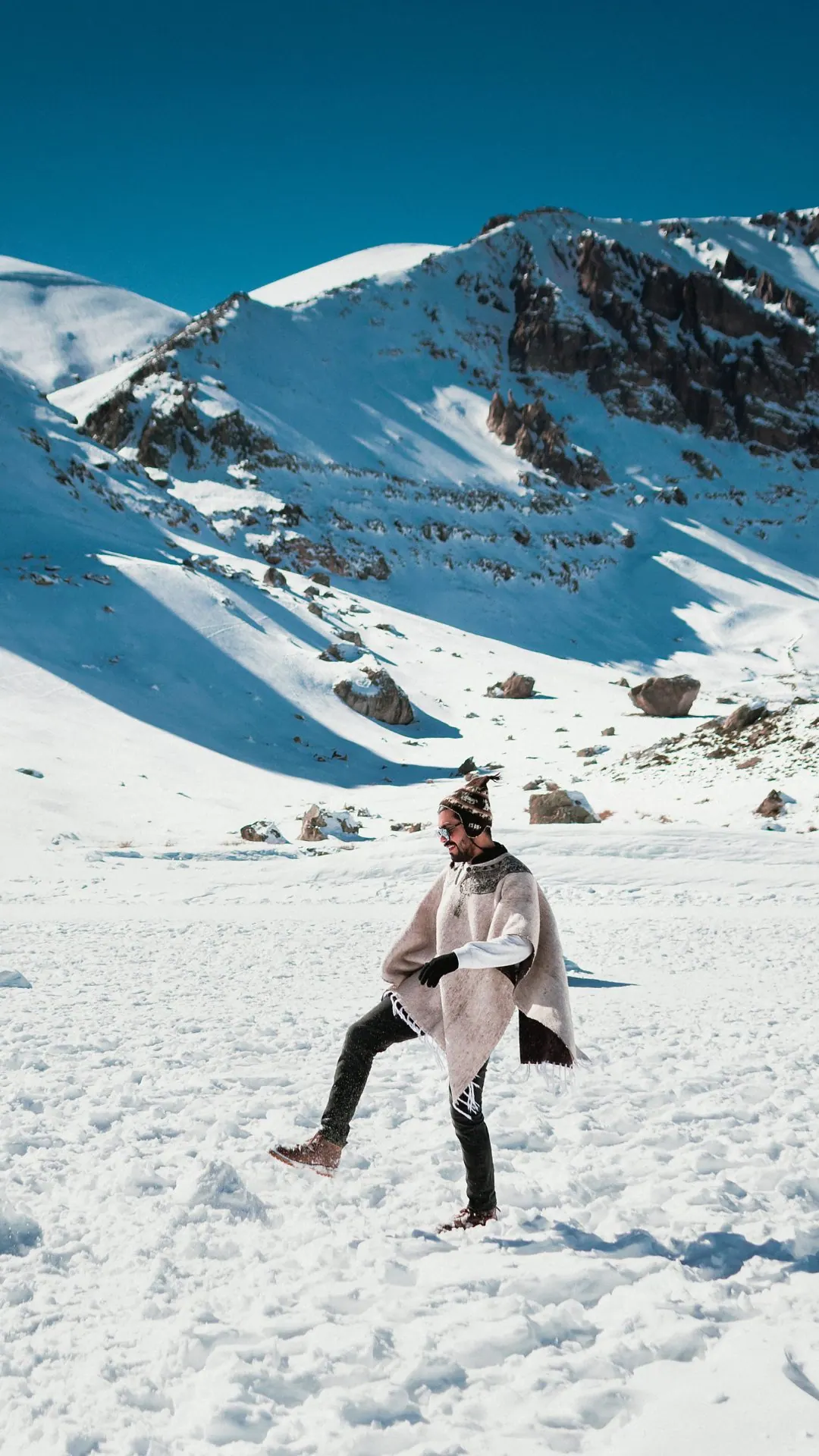 Viajante com poncho brincando na neve da Cordilheira dos Andes